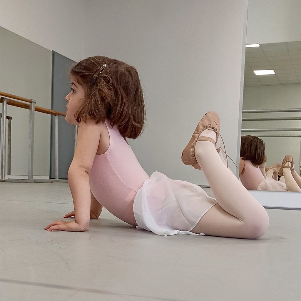 Niña alumna de predanza (3 a 6 años) realizando un ejercicio de estiramiento en clase de ballet en Madrid Río Escuela de Danza